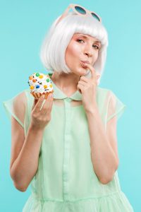 graphicstock happy playful young woman in blonde wig tasting cupcake by finger over blue background SufVPiHne